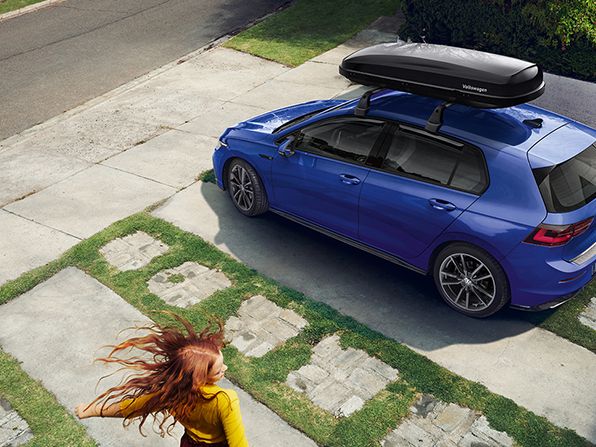 Ein blauer VW Golf mit Dachbox parkt vor einer Hauseinfahrt